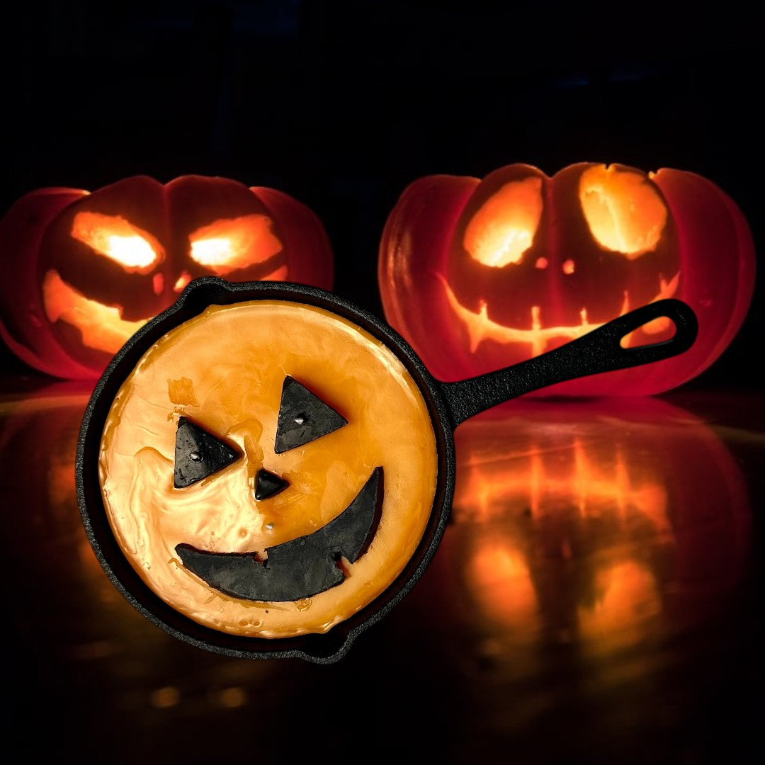 Doodlations unique candle in a cast iron skillet, shaped like a jack o’ lantern with orange wax and black facial features.