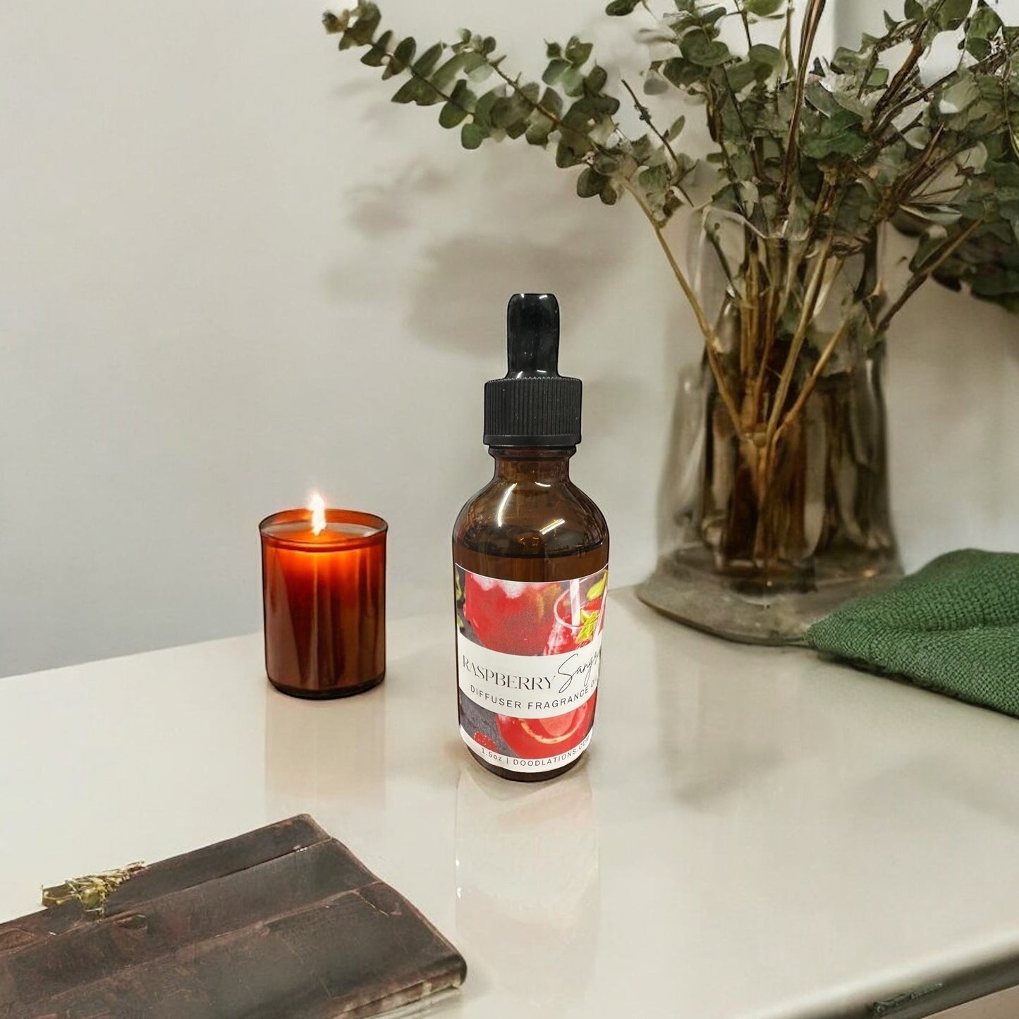 Doodlations Coffee Bar & Boutique Raspberry Sangria fragrance oil in amber dropper bottle with lit candle and eucalyptus.