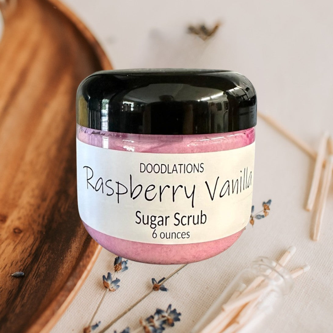 Doodlations Raspberry Vanilla Sugar Scrub in a clear jar with a black lid, pink scrub inside.
