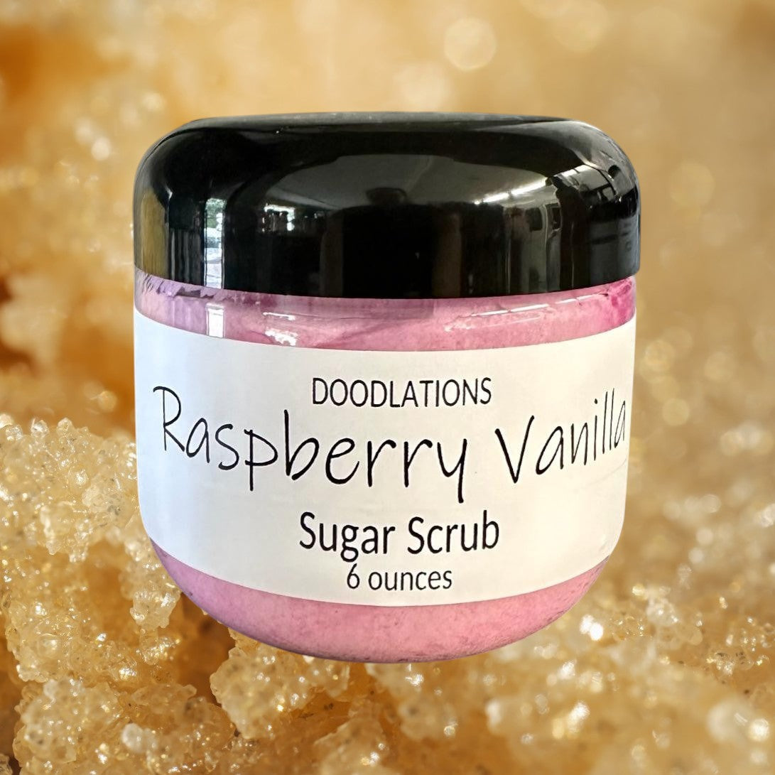 Doodlations Raspberry Vanilla Sugar Scrub in a clear jar with a black lid, pink scrub inside.