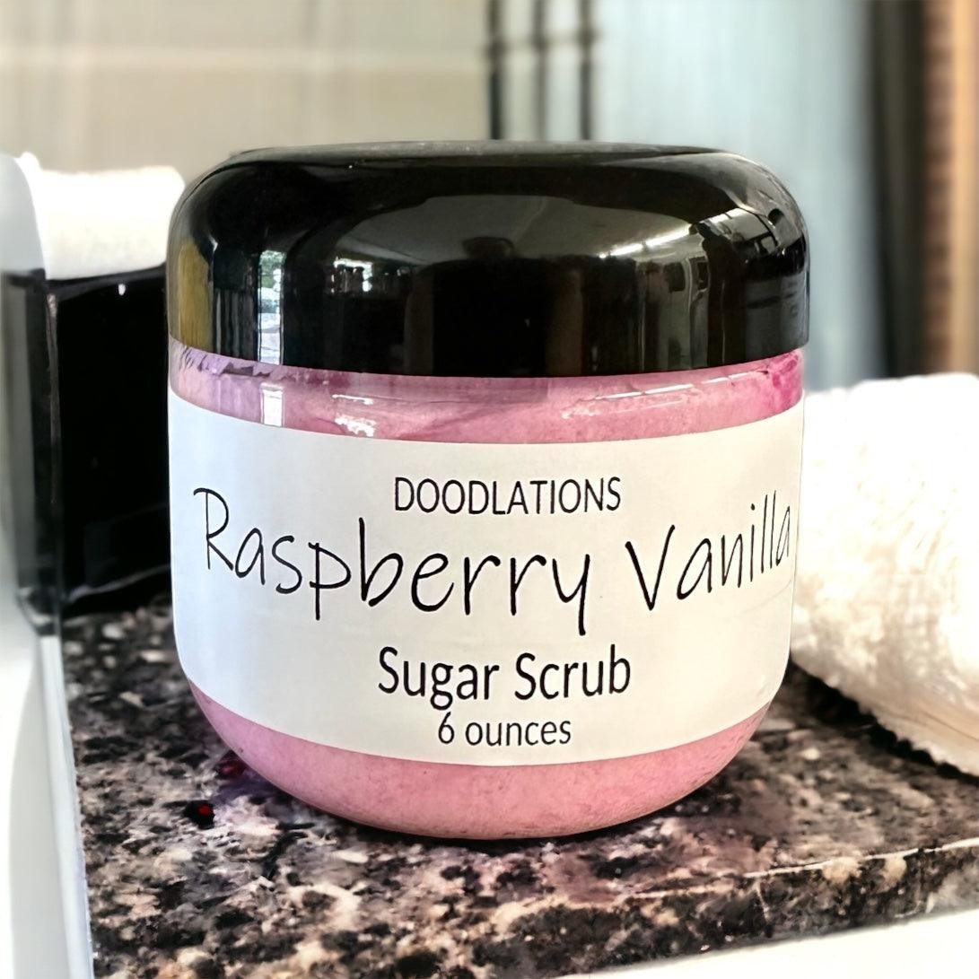 Doodlations Raspberry Vanilla Sugar Scrub in a clear jar with a black lid, pink scrub inside.