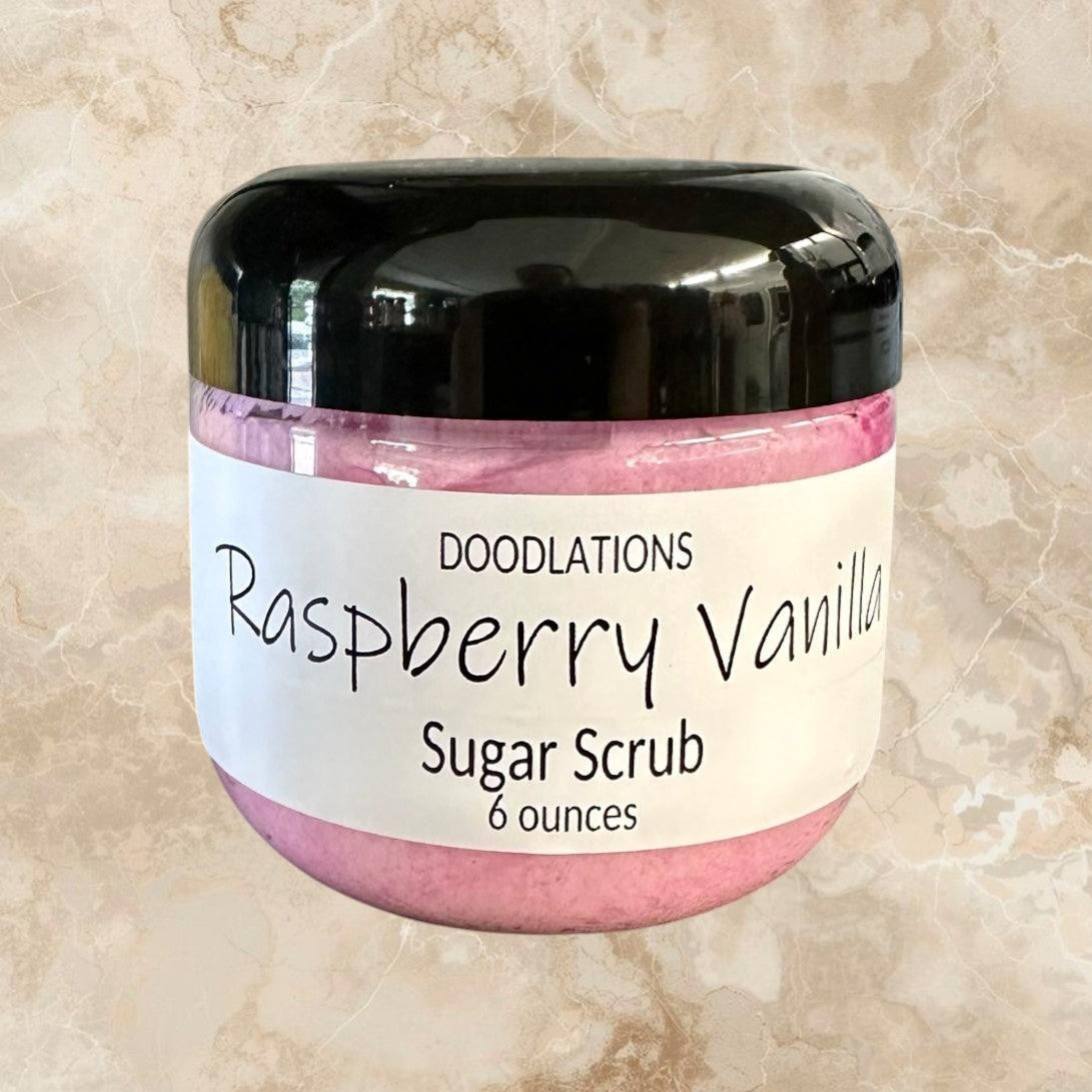 Doodlations Raspberry Vanilla Sugar Scrub in a clear jar with a black lid, pink scrub inside.