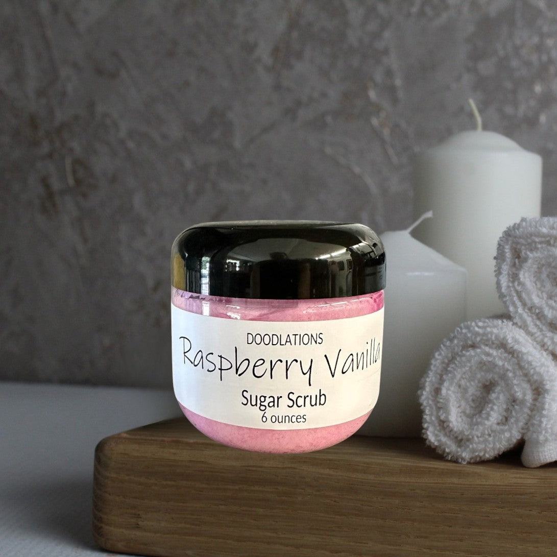 Doodlations Raspberry Vanilla Sugar Scrub in a clear jar with a black lid, pink scrub inside.