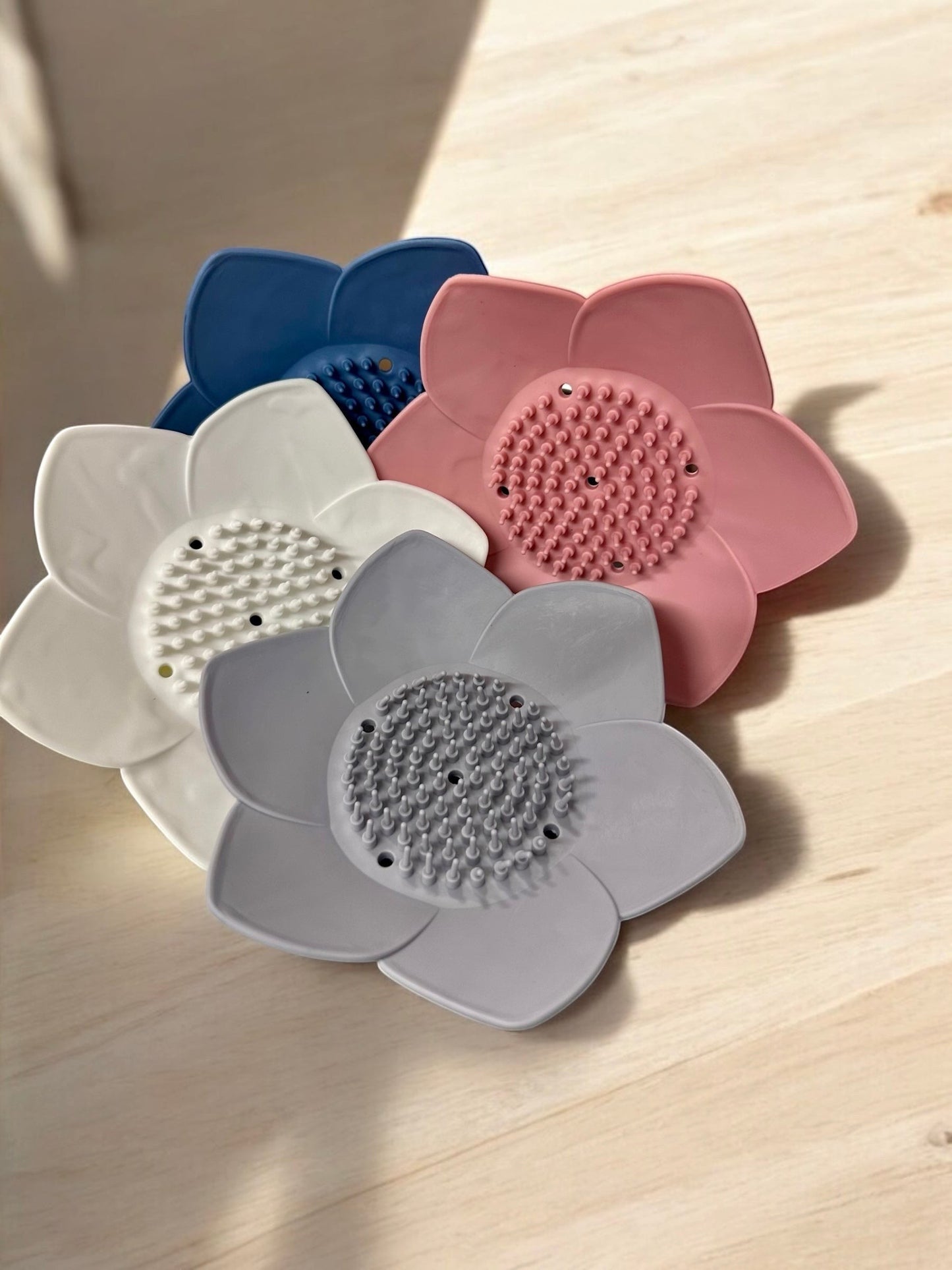 Doodlations Coffee Bar & Boutique silicone lotus flower shower steamer holder in blue, pink, white, and grey. Features textured center for grip.