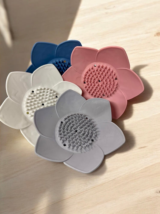 Doodlations Coffee Bar & Boutique silicone lotus flower shower steamer holder in blue, pink, white, and grey. Features textured center for grip.