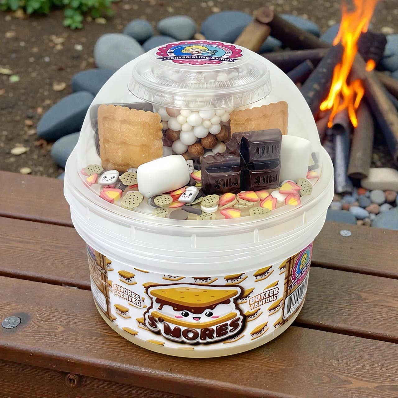 Doodlations Smores Scented Slime bucket with marshmallow, chocolate, and graham cracker add-ins. Campfire background.
