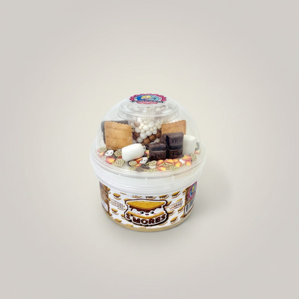 Doodlations S'mores Slime: A clear container filled with various s'mores-themed charms, including chocolate bars, marshmallows, graham crackers, and sprinkles.