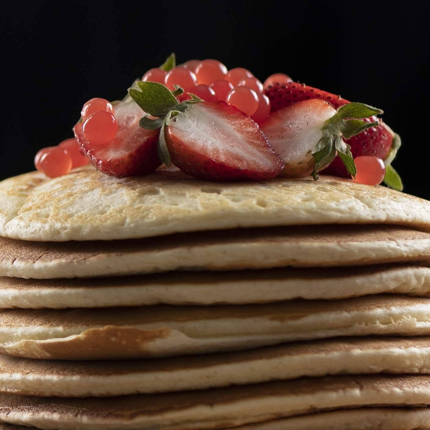 Doodlations Coffee Bar & Boutique strawberry bursting balls topping fresh strawberries on a stack of pancakes.