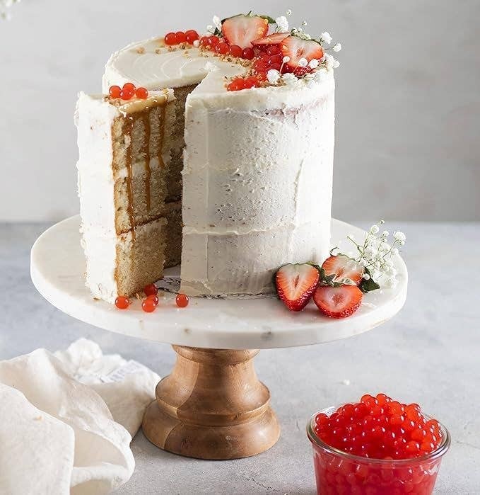 Doodlations Coffee Bar & Boutique Strawberry Bursting Balls topping a white frosted cake with fresh strawberries and caramel drizzle.