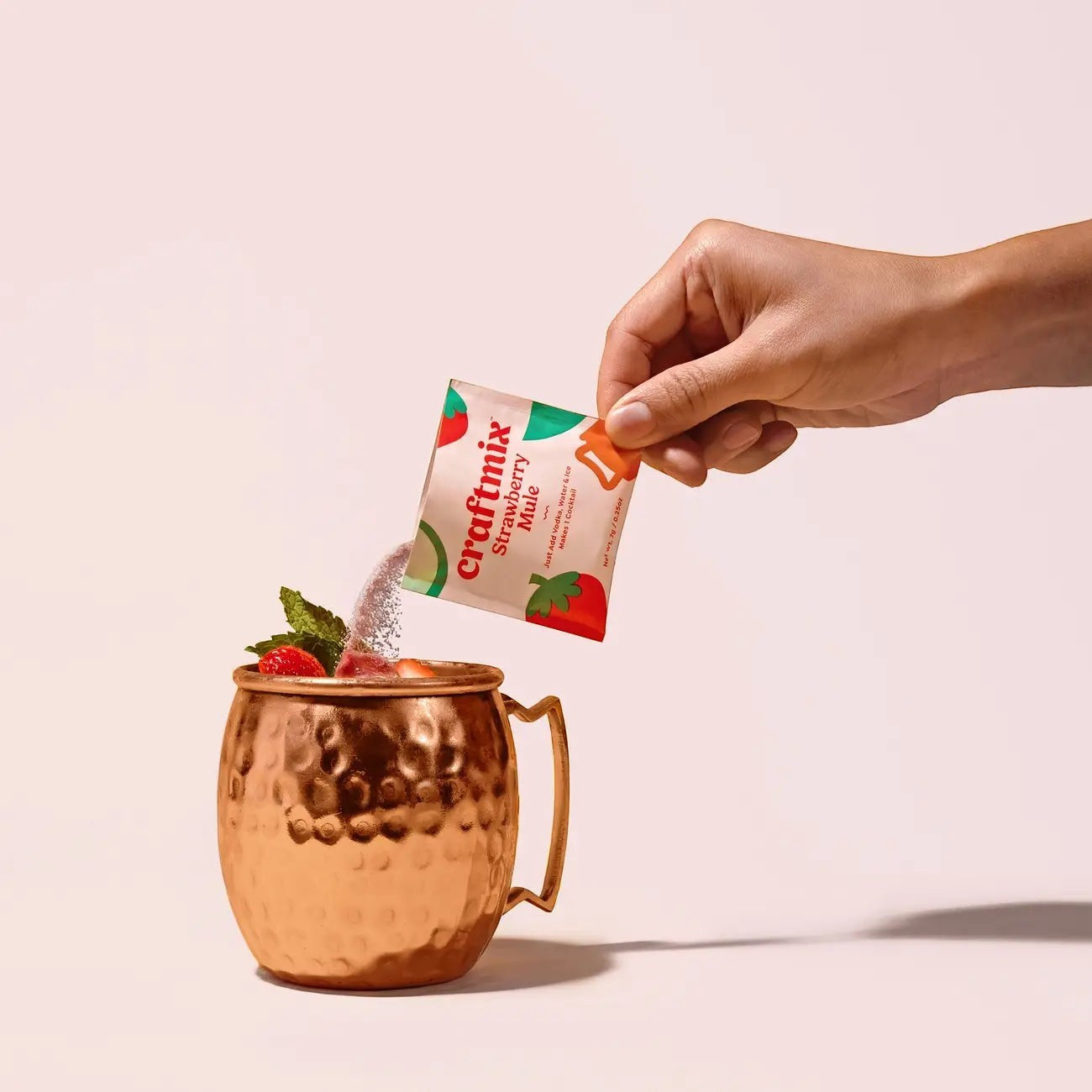 Doodlations Coffee Bar & Boutique Craftmix Strawberry Mule mixer packet being poured into a copper mug with strawberries and mint.