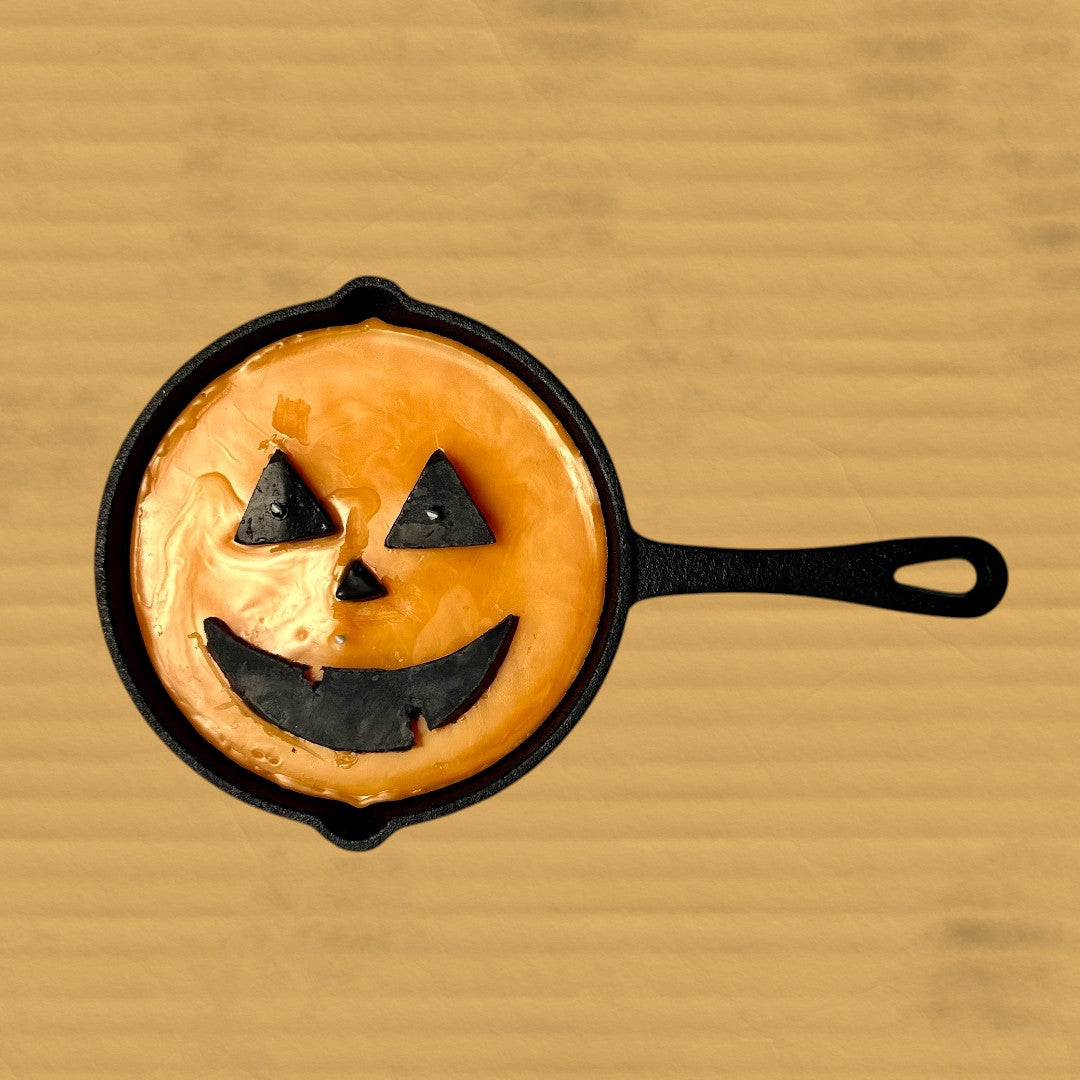 Doodlations Unique Candle in a cast iron skillet shaped like a smashed pumpkin Jack O’ Lantern. Orange wax with black face details.