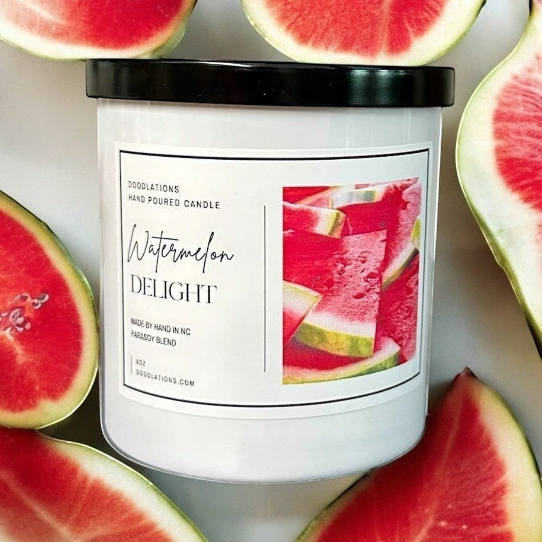 Doodlations Watermelon Delight hand-poured soy blend candle in a white jar with a black lid, surrounded by fresh watermelon slices.