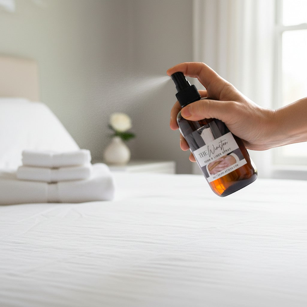Doodlations Coffee Bar & Boutique The Winston Room & Linen Spray bottle being sprayed on a white bed. Notes of tobacco, honey, amaretto, and oak.