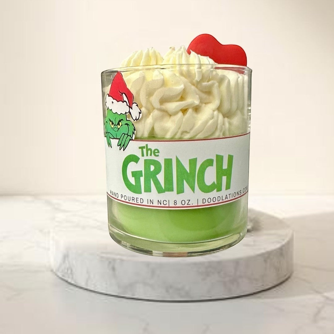 The Grinch candle with green wax and white whipped wax topping, decorated with a Grinch sticker and red heart.